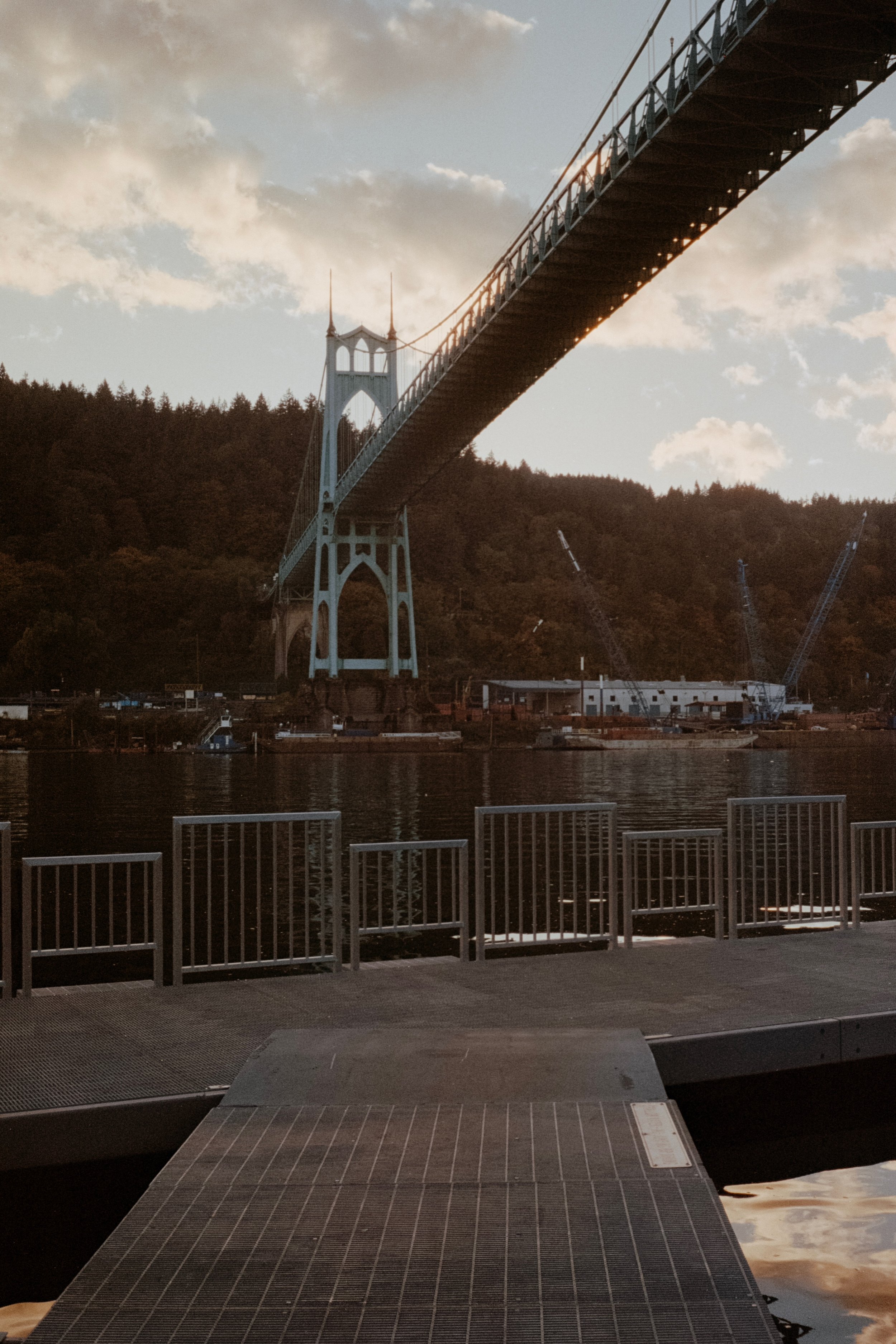 The St. Johns Bridge viewed from a dock, with the sun glowing through its structure and the water reflecting soft evening light.
