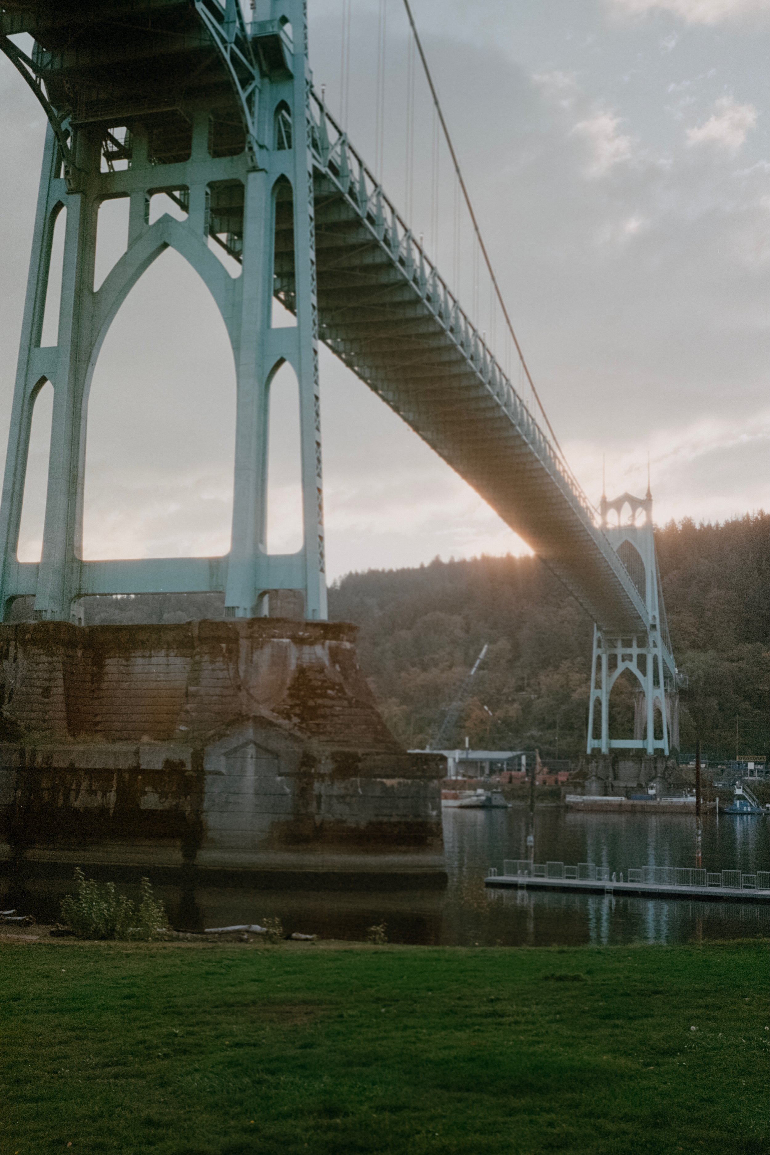 The St. Johns Bridge viewed from underneath with sunlight glowing as it sets over distant hills.
