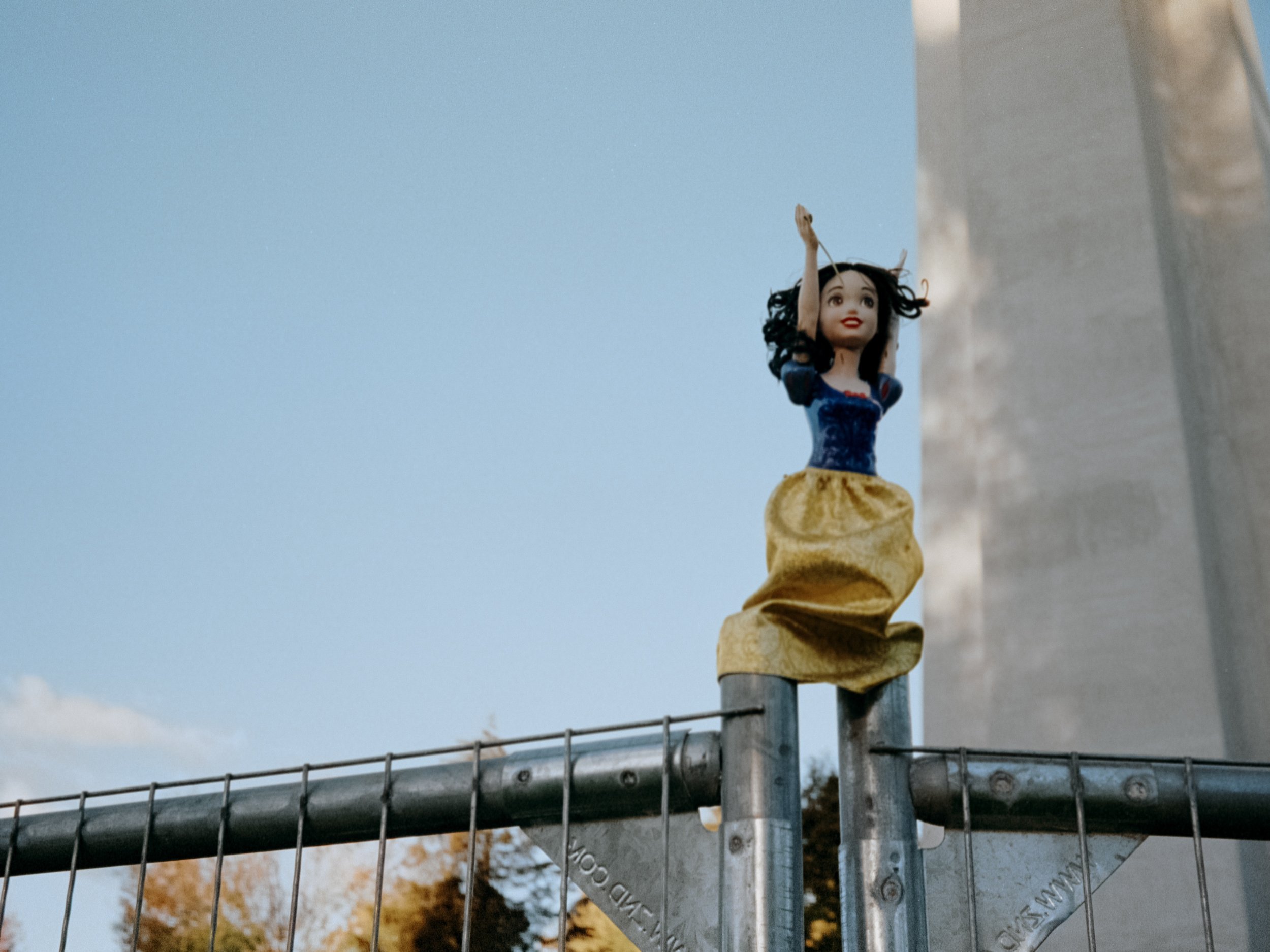 A Snow White doll with a knife, perched atop a metal fence.