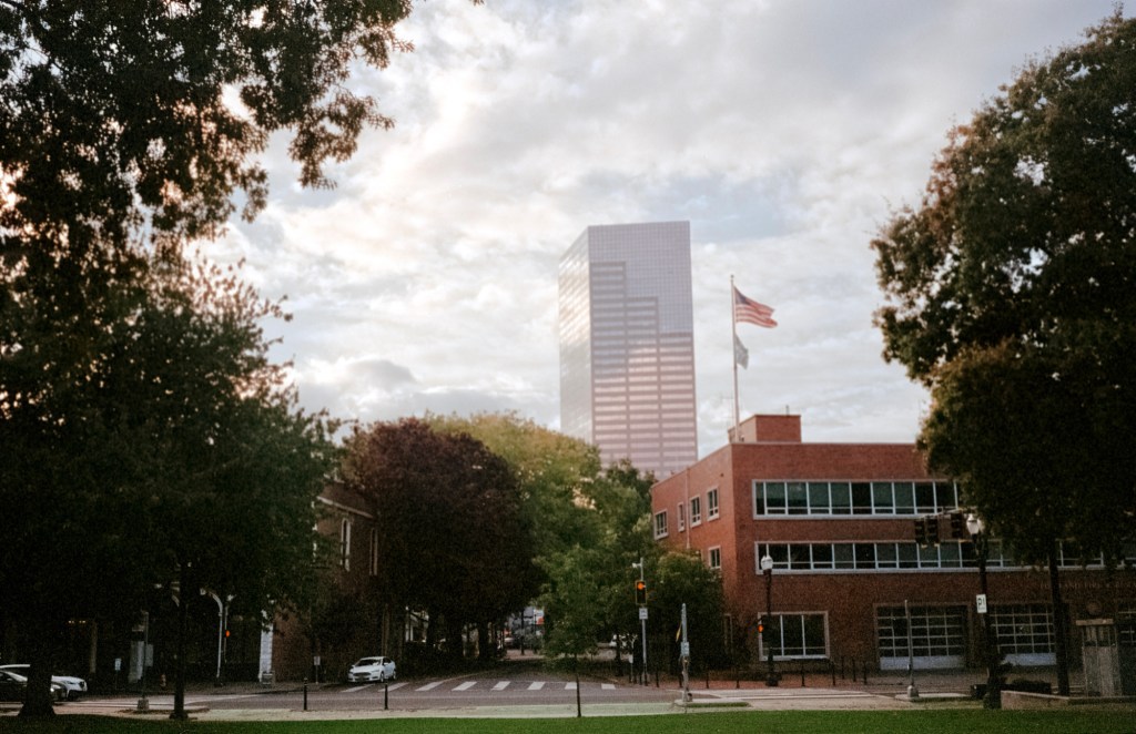The US Bancorp Tower in the background, with an American flag flying above a red brick building and tree-lined street in Portland, Oregon.