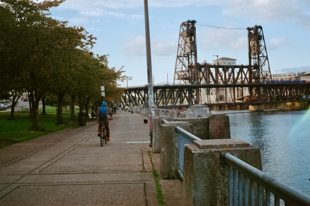 Cyclist riding through South Waterfront Park in Portland, Oregon, with the Steel Bridge in the background.