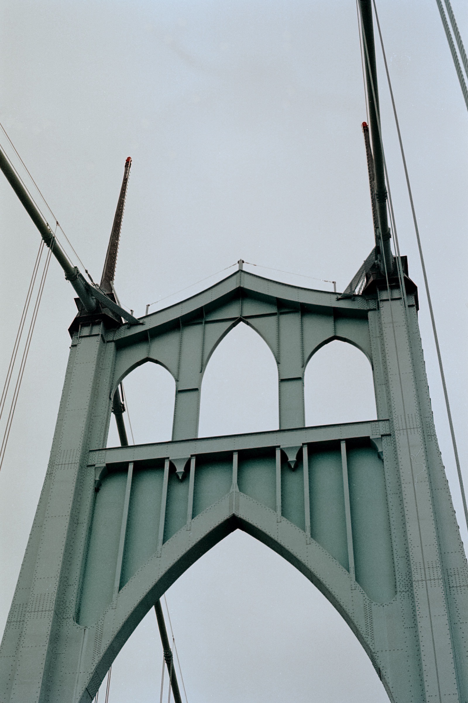 A close-up of the St. Johns Bridge’s Gothic-style tower and spires, showcasing its green steel framework against a cloudy sky.