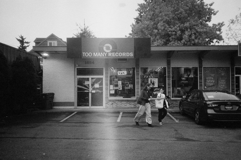 Black-and-white photo of two women in parking lot in front of Too Many Records in Portland, Oregon.