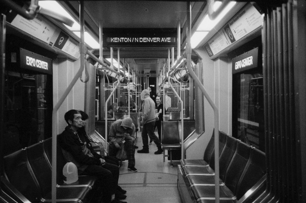 Inside of a Portland MAX train with older couple sitting on the left and people standing in the background.