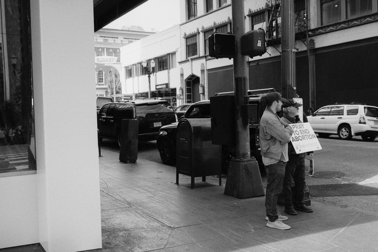 Black-and-white photo of two anti-abortion activists on a street corner.