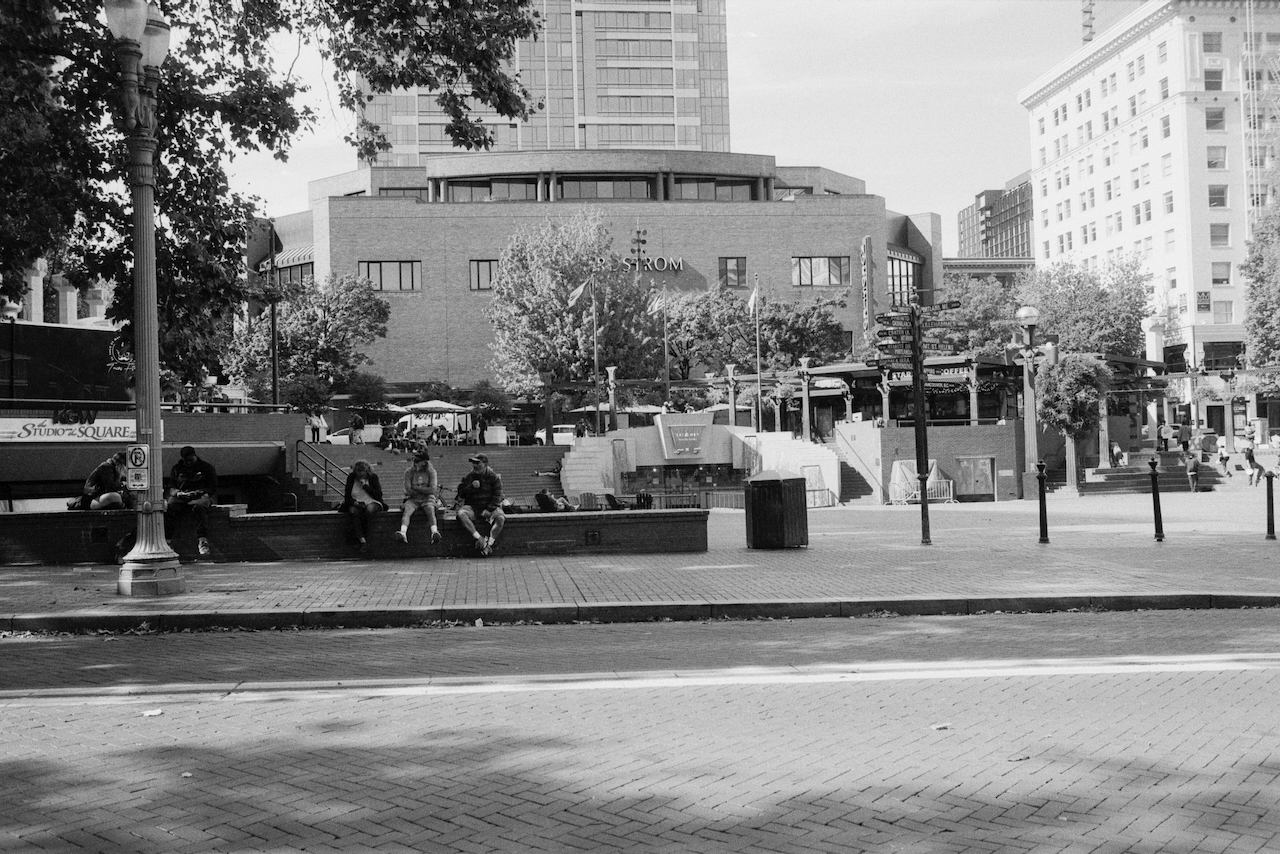 Black-and-white photo of people sitting across the street in front of Pioneer Square in Portland, Oregon.