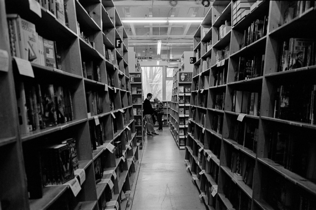 Black and white photo of two people at the end of a long aisle of books.