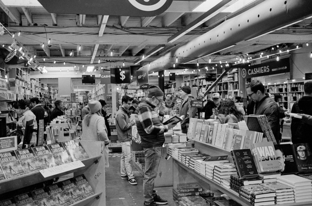 A busy day in the front of a book shop with people browsing and checking out.